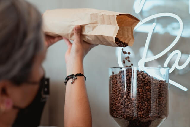 A barista adding coffee beans to a coffee grinder