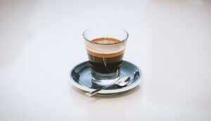 A clear glass cup of espresso on a saucer, showcasing the rich color and texture of a home-brewed espresso.
