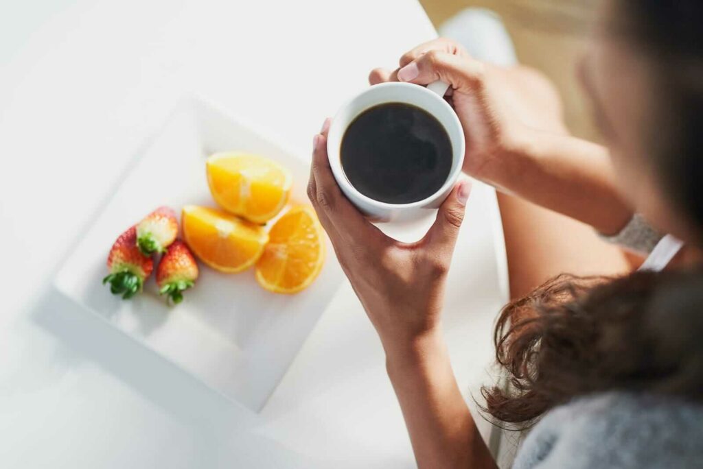 A person holds coffee above fruit plate
